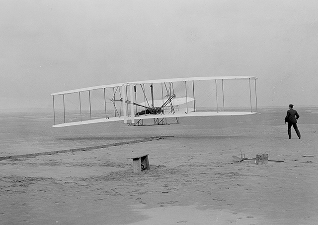 The iconic image of Orville Wright’s first flight with Wilbur running alongside the right wing as the craft broke earth’s gravity near Kitty Hawk, North Carolina, almost didn’t happen. Coast Guardsman John T. Daniels was thrust into the limelight when he was tasked with operating Wilbur’s boxy Korona-V glass-plate camera to document the Wright brothers flight into history Dec. 17, 1903. Photo by John T. Daniels.